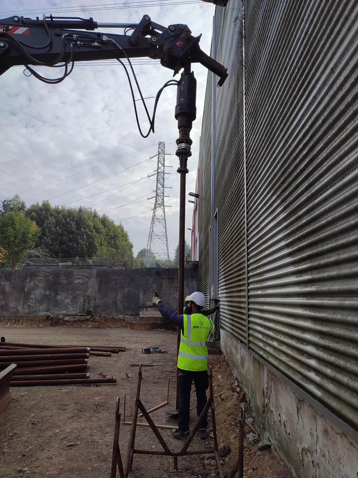 Helical pile installation next to a warehouse facade